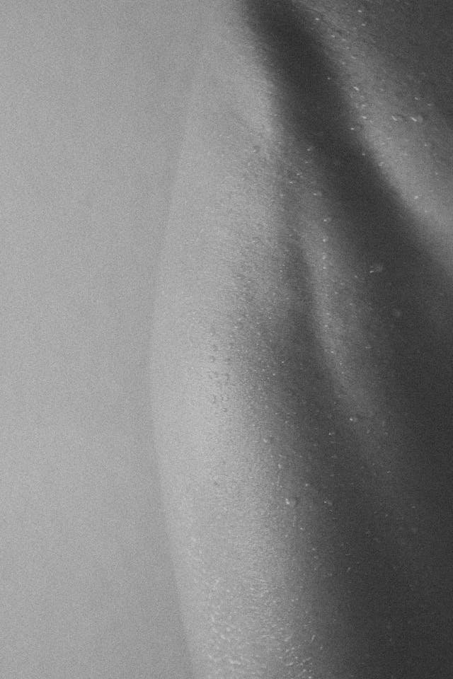 Primo piano in bianco e nero di un corpo femminile bagnato, con gocce d’acqua sul torace.