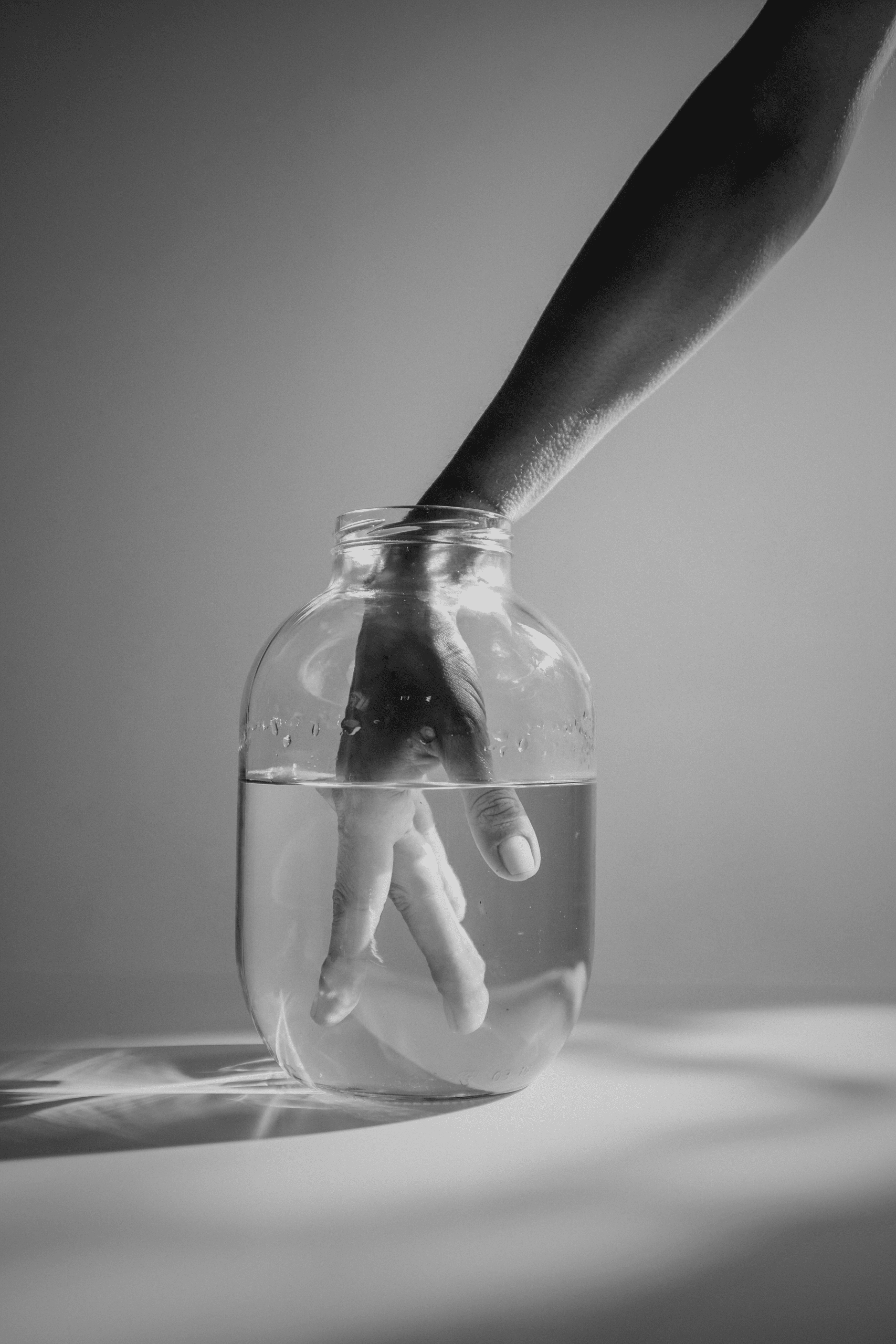 Mano immersa in un barattolo di vetro con acqua, in bianco e nero.