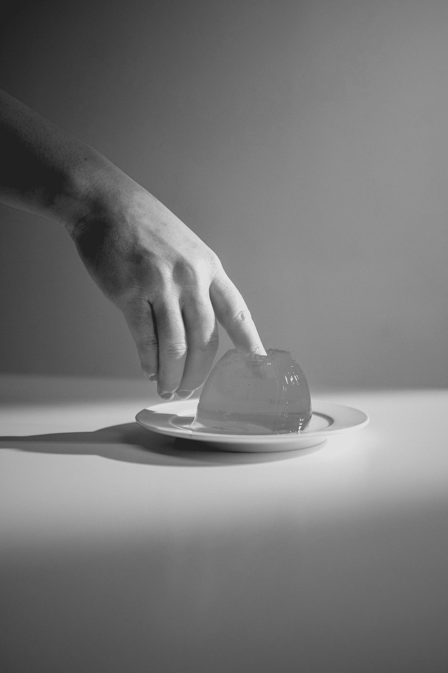 Mano femminile che immerge le dita in un pezzo di gelatina trasparente su un piattino, in bianco e nero.