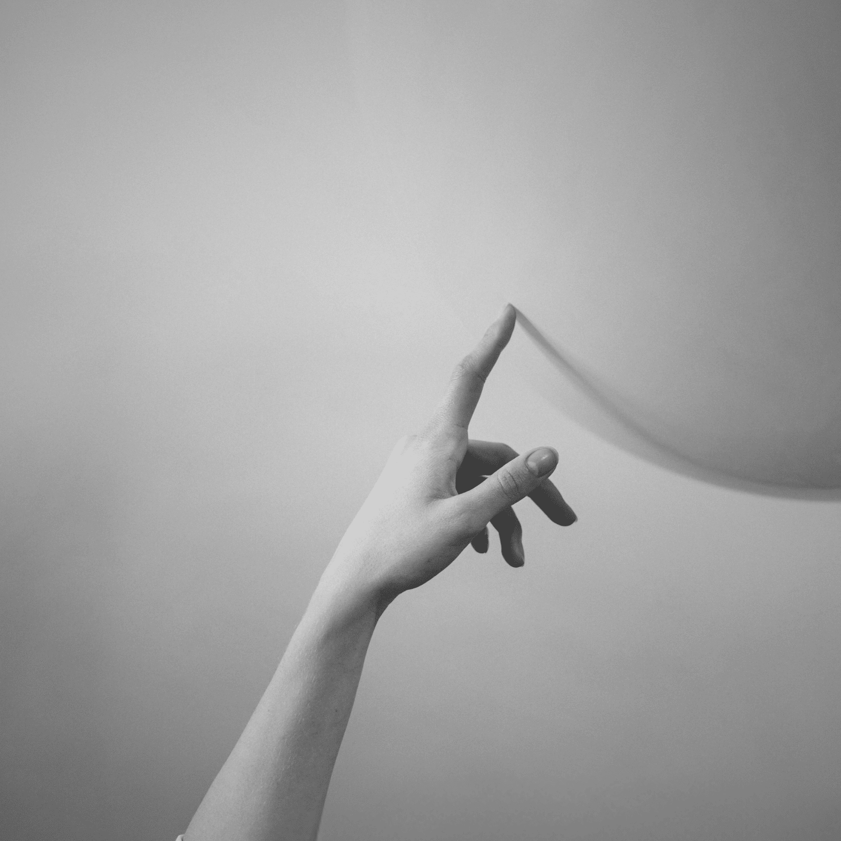 Mano femminile che sfiora delicatamente un palloncino, in bianco e nero.