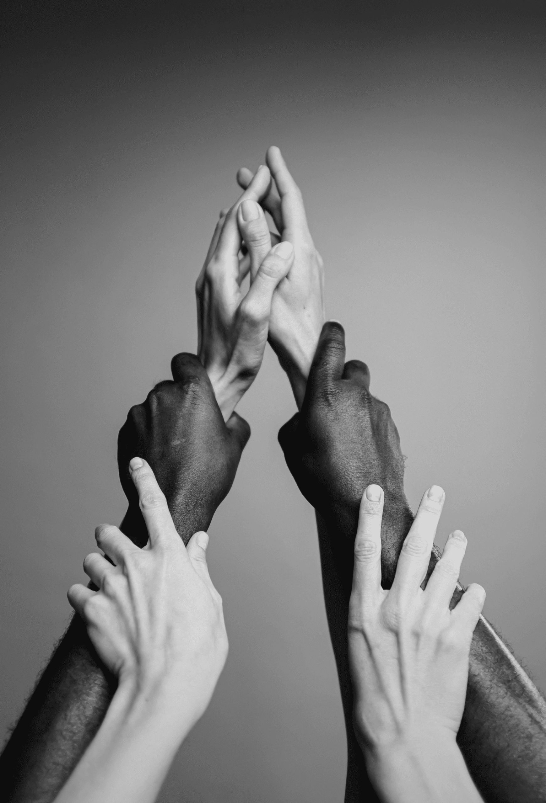 Mani di più persone che si uniscono verso l’alto, immagine in bianco e nero.