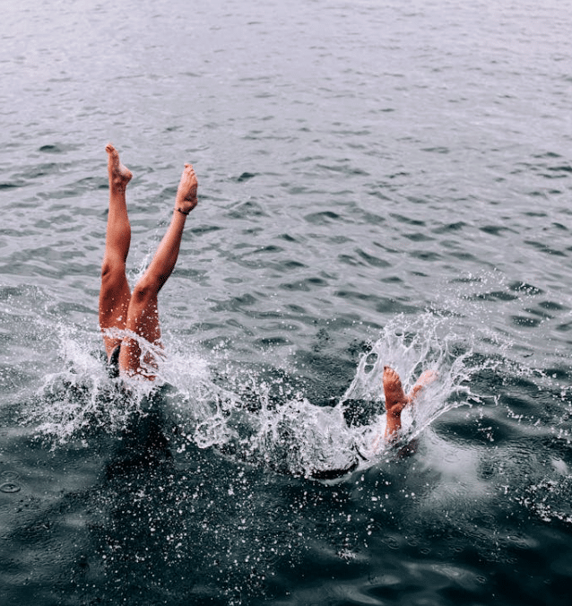 Donne che si tuffano nell’acqua con le gambe in aria e schizzi intorno.